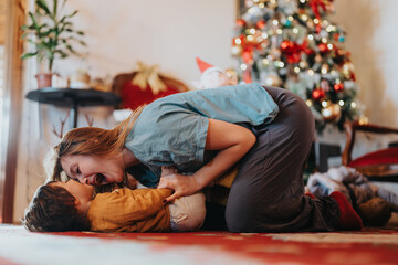 A playful interaction between a parent and child near a beautifully decorated Christmas tree,...