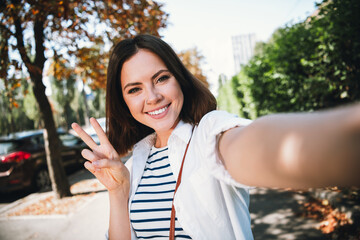 Young woman smiling in natural light on a sunny day, wearing stylish casual shirt, enjoying leisure...