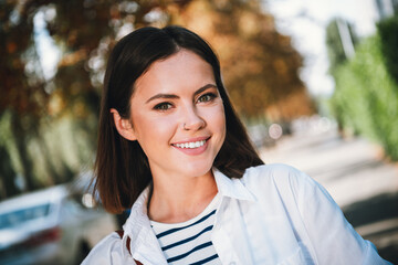 Charming young woman enjoying a sunny day in autumn, walking outdoors with a smile in casual clothes
