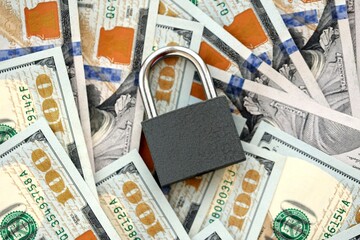 Small black padlock lies on big amount of new hundred US dollar bills