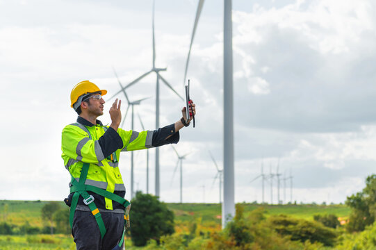 man in  yellow and black safety vest is taking apicture of  wind farm