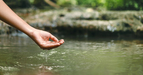 hand is reaching into  body of water, possibly  river or  pond