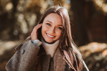 Beautiful attractive woman enjoying an autumn day in the park, wearing a coat, smiling warmly under...