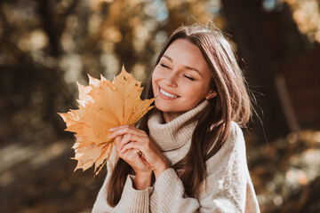 Chic young woman enjoying a bright autumn day with golden foliage in the park, radiating happiness and elegance.
