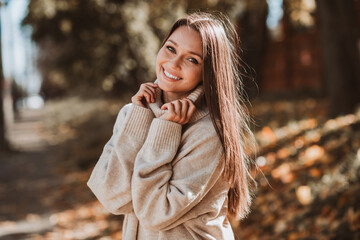 Smiling young woman in casual autumn outfit enjoying a sunny walk in a park filled with vibrant...