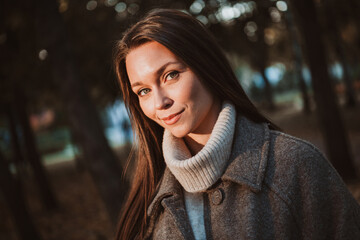 A young woman enjoying a relaxing walk in an autumn park, bathed in warm daylight, showcasing...