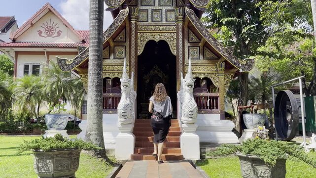 Tourist entering Wat Phra Singh temple in Chiang Mai, Thailand, with ornate golden architecture, guardian statues, and traditional Lanna design