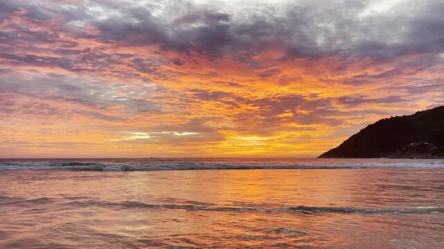 Panoramic view of golden sunset over Nai Harn Beach, Phuket, Thailand, with dramatic clouds, calm waves, and glowing reflections across the sea at twilight