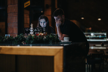 Two individuals intently focused on a computer work together in a warmly lit cafe, surrounded by Christmas decorations, creating a professional yet festive atmosphere.