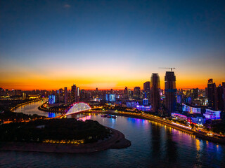 Fototapeta premium Wuhan city in China presents a radiant evening skyline along the Yangtze River, with colorful lights illuminating modern buildings and a bright bridge reflecting on the water.