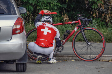 A cyclist adjusts a bicycle by the side of the road on a summer day