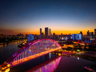 Fototapeta premium Wuhan China cityscape showcases a beautifully illuminated bridge crossing the Yangtze River, with its vibrant lights reflecting on the water, shining brightly under the twilight sky.