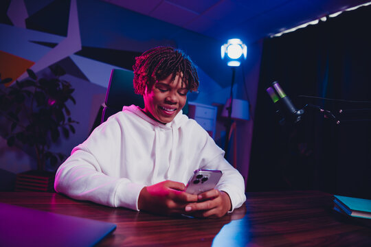 Positive man in a neon-lit room using smartphone while podcasting with microphone showcasing creative online engagement