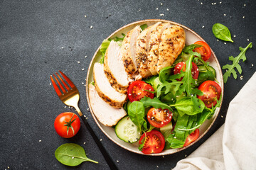 Green salad with grilled chicken meat at black table.