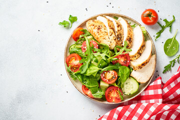 Green salad with grilled chicken meat at black table.