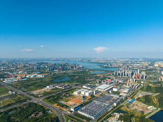 Fototapeta premium An aerial view captures the vast urban landscape of Jiangxia, Wuhan, featuring modern buildings, clear lakes, green areas, and busy roads under a bright blue sky.