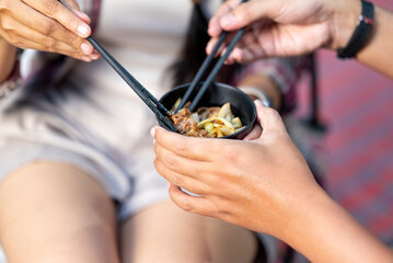 Couple sharing food with chopsticks. Smiles and enjoying togetherness while camping outdoors. The scene of the lifestyle of enjoying food in a natural setting