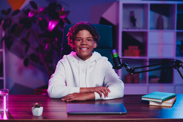 Young content creator sitting at a desk with microphone in a modern studio setup, browsing online content in evening