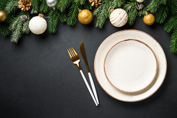 Christmas table setting. Craft plates with cutlery and golden christmas decorations at black.
