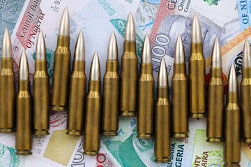 Nigerian naira currency money bills and rifle bullets close up. The concept of warfare and gun...