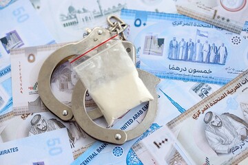 United Arab Emirates dirham currency money bills and cocaine pack with handcuffs close up. The...