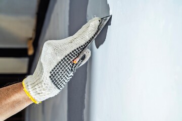Construction worker in gloves using a scraper to fill cracks and surface imperfections on the wall...