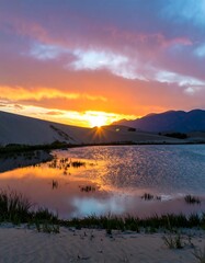 Fototapeta premium A breathtaking sunset paints the sky with vibrant hues over a tranquil desert pool, reflecting the golden light on the calm water.