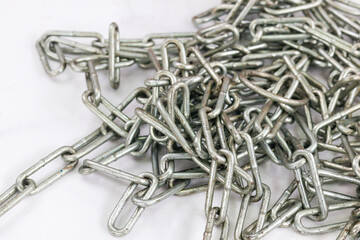 A tangled pile of industrial metal chain links on a white surface. The close-up detail highlights...