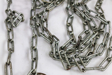 A tangled pile of industrial metal chain links on a white surface. The close-up detail highlights...