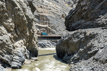 A green 4x4 motorhome crossing a bridge in the middle of a large canyon.