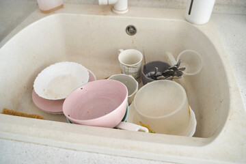 Dirty dishes in white kitchen sink with plates, mugs, and cutlery.