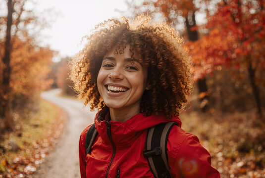 Cheerful traveler in red jacket enjoying sunny autumn day on forest path surrounded by vibrant foliage - Powered by Adobe