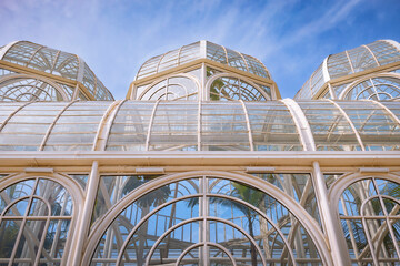 The metallic arch structure, with curved glass panels, forms the central dome of the botanical greenhouse under the blue sky.