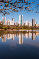 Urban view of the city of Londrina, Brazil, with a lake in the foreground, a strip of vegetation in the middle, and residential skyscrapers in the background.