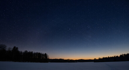 Fototapeta premium Night Sky over Lake: A mesmerizing long exposure photograph captures the tranquil beauty of a star-studded night sky mirrored on a glassy lake's surface, with a silhouetted tree line on the horizon.