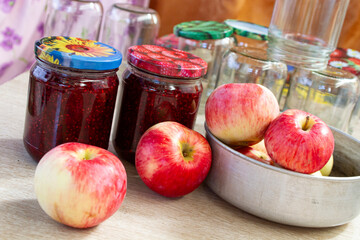 red and yellow apples on the table next to jars of raspberry jam and empty glass jars in the background