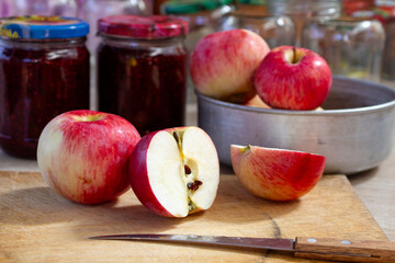 red and yellow apples on the table next to jars of raspberry jam and empty glass jars in the background