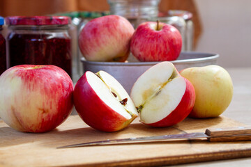 red and yellow apples on the table next to jars of raspberry jam and empty glass jars in the background