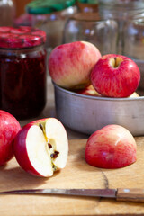 red and yellow apples on the table next to jars of raspberry jam and empty glass jars in the background