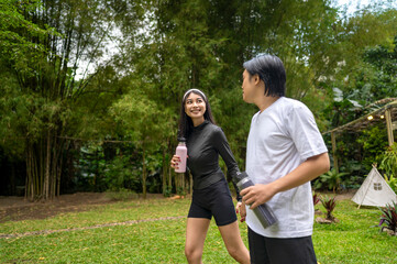 Naklejka premium Indonesian southeast asian couple in a sporty outfit holding a drink bottle while practicing running exercise together in a public park outdoors. Concept of a Healthy active lifestyle