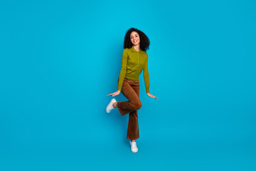 Young woman wearing casual retro-style outfit posing playfully against a vibrant blue background...