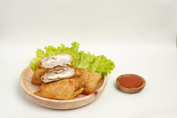 Close up of fried dimsum with melted cheese filling, served on a wooden plate with fresh lettuce and chili sauce.