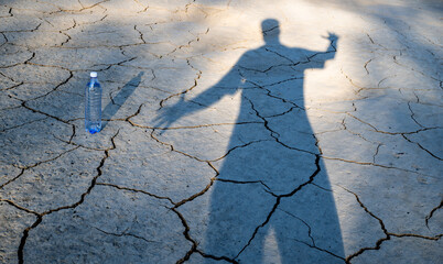 A bottle of drinking water, a man's shadow and clay cracked by the heat in the desert