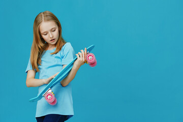 A young girl with long hair wearing a blue shirt examines her turquoise skateboard on a vibrant...