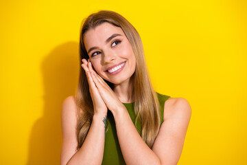 Smiling young woman with hands clasped in a charming pose, wearing a green top in front of a vivid...