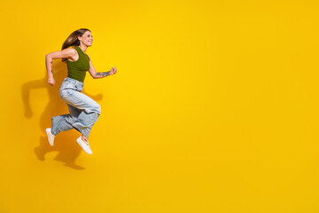 Young woman in casual attire happily jumping against a vibrant yellow background expressing energy...