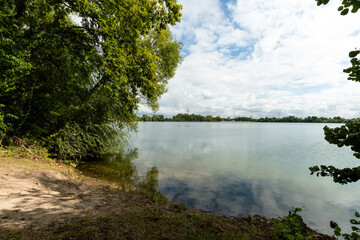 Ein ruhiger Sommersee mit klarem, stillen Wasser und grünen Bäumen, die sich über das Ufer...