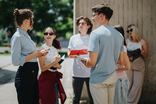 Young students with a professor interacting and working on academic tasks outdoors, representing education, team collaboration, and outdoor study activities in an engaging and supportive setting.