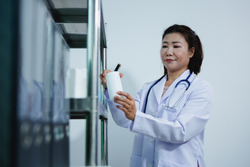Asian female pharmacist is preparing medicine for patient and giving advice on proper use of...