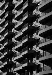 Obraz premium Close-up view of modern high-rise apartment building with repetitive balcony design and metal railings in black and white photography